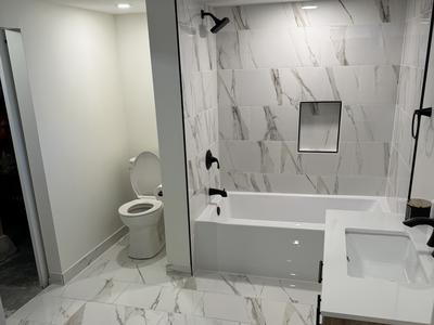 Marble-look tile tub and shower surround with matte black fixtures and quartz vanity