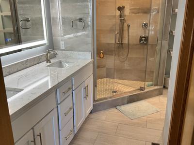 Master bathroom with white double vanity, backlit mirror and glass shower enclosure