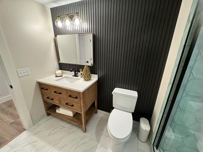 Bathroom with black slat accent wall, wood vanity and gold framed mirror