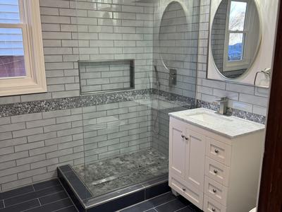 Walk-in shower with gray subway tile, pebble accent band and glass panel