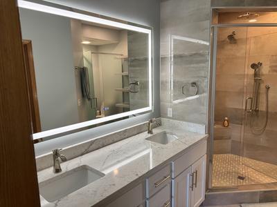 Double vanity with marble countertop, backlit mirror and tiled walk-in shower