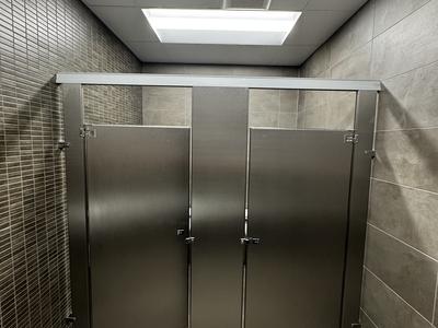Commercial restroom with porcelain tile walls and stainless steel partitions